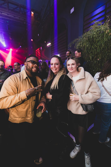 Drei lächelnde Personen auf einem Event mit Bühnenbeleuchtung.