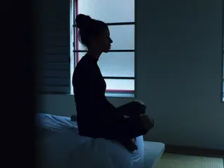 A woman meditating near a window using a wearable headset