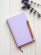 light wood table top with an angled lavender notebook, gold pen. Make the notebook off to
