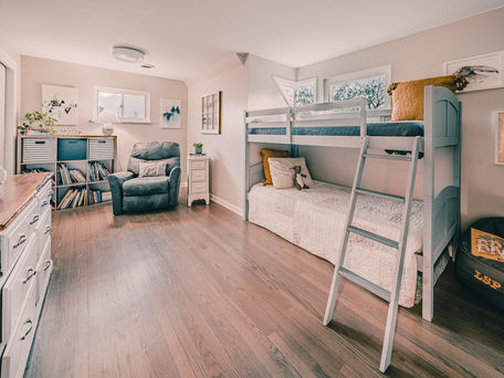 A renovated children's room with a hand built bunk bed, walnut wooden floors, a blue recliner in the corner with a yellow pillow. On the left side of the room there is a white dresser
