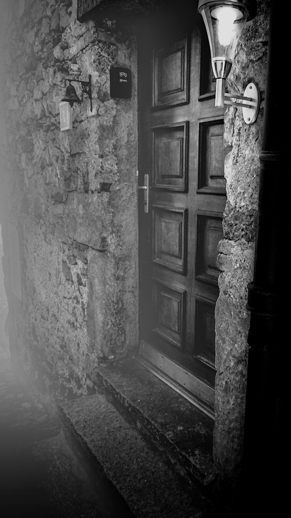 Black and white fine art photograph of an old wooden door set in a stone wall, illuminated by vintage lantern light