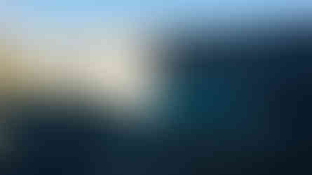 Volcanic crater with vibrant turquoise lake, surrounded by rugged, rocky cliffs. Thick mist rises from the water against a clear sky.