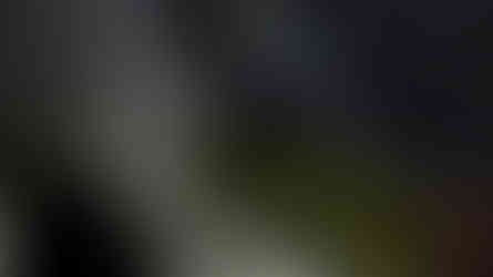 Blue flames rise from a rocky surface at night, surrounded by smoke. People in winter hats watch, some using phones to capture the scene.