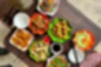 Colorful plates of various fried and fresh foods on a dark wooden table, with chopsticks, dipping sauces, and empty bowls nearby.