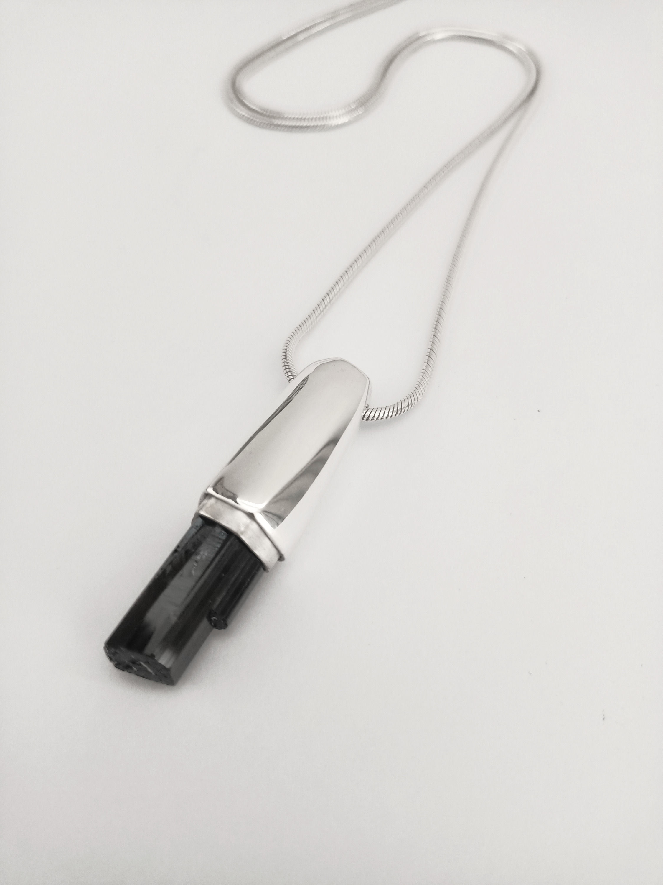 Unisex pendant featuring raw onyx in a sculptural silver setting on a snake chain on white background.