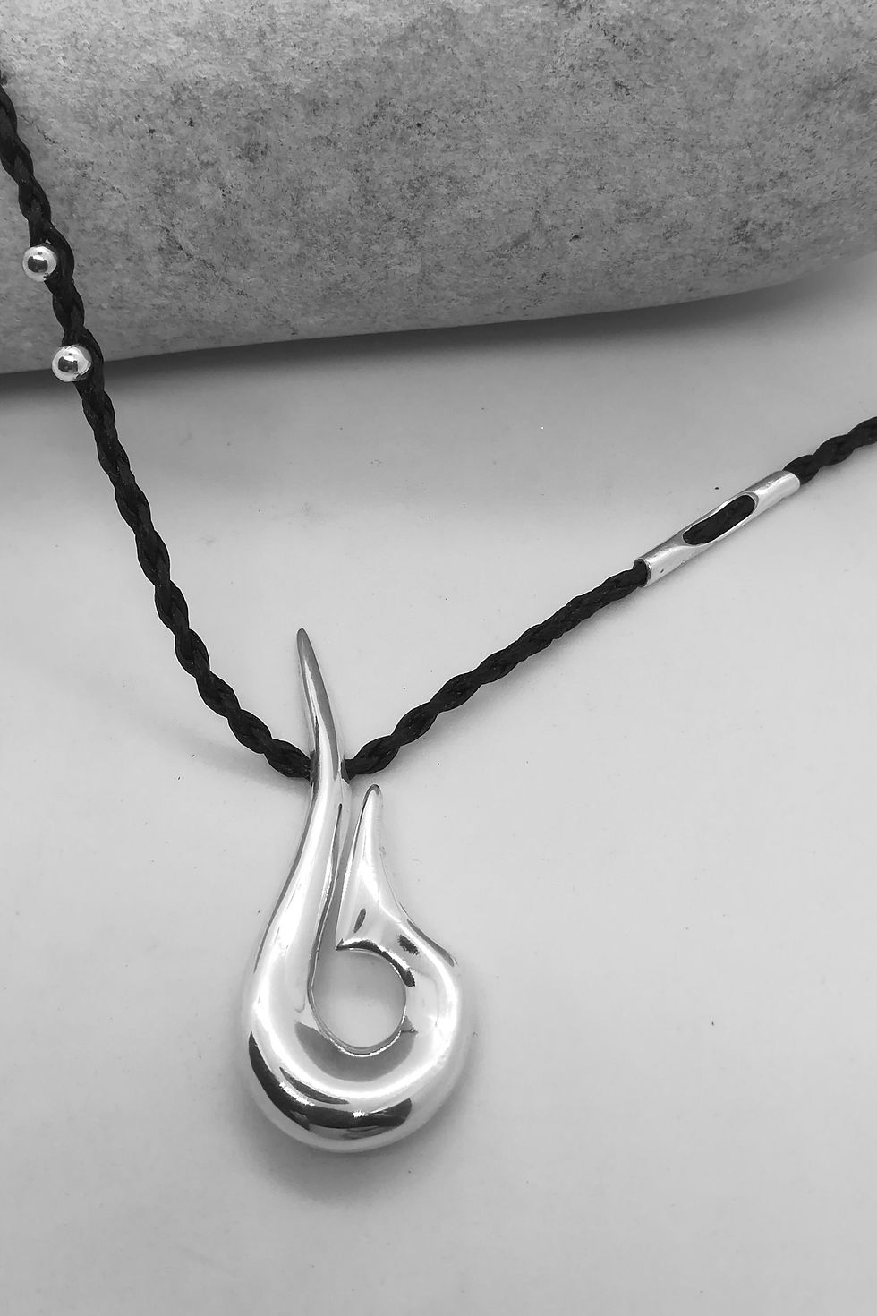 Sculptural silver flame pendant laid flat beside a stone on white background.