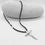 Thumbnail: A sculptural silver cross pendant on black cord displayed on smooth white stone.