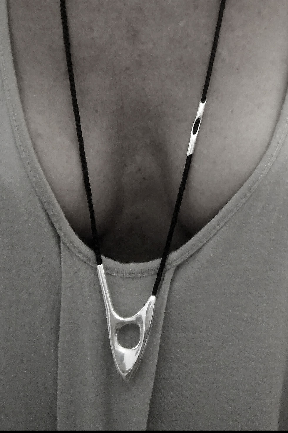 Close-up of a person wearing the ORYXA silver pendant with a deep neck top, showcasing it's sleek, sculptural form.