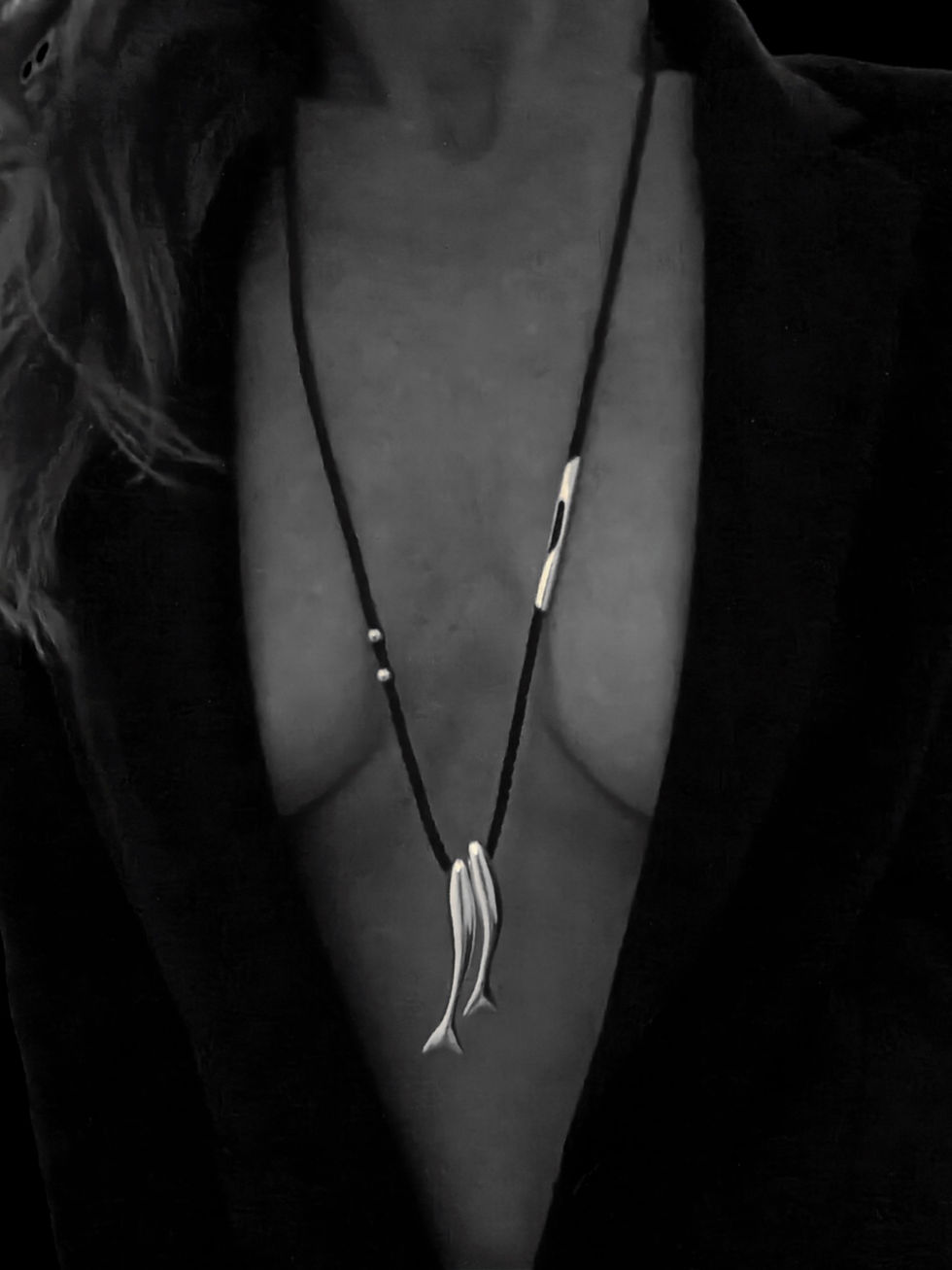 Black and white photo of model wearing the DELPHI DUO silver dolphin pendant on a black cord necklace.