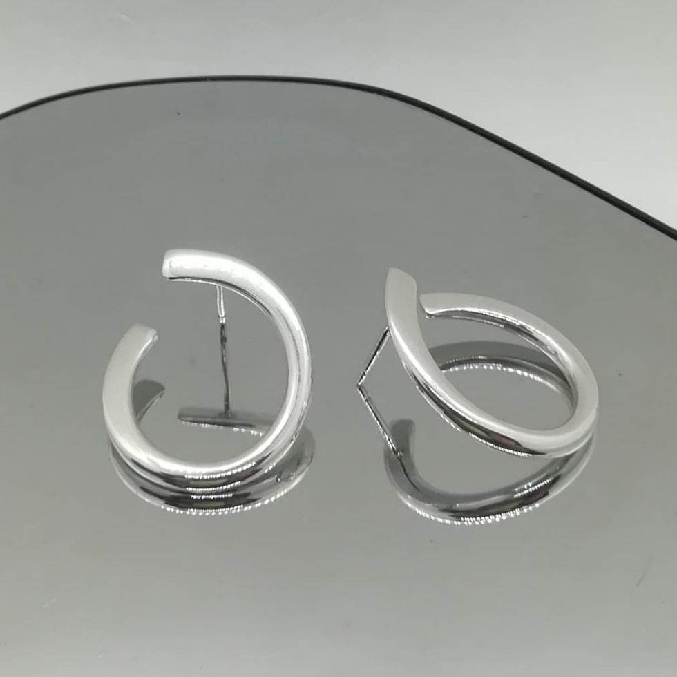 Studio image of sculptural twisted silver hoop earrings on mirrored surface.
