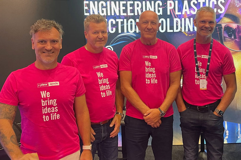 Fire smilende ansatte i rosa t-skjorter foran en stand.
