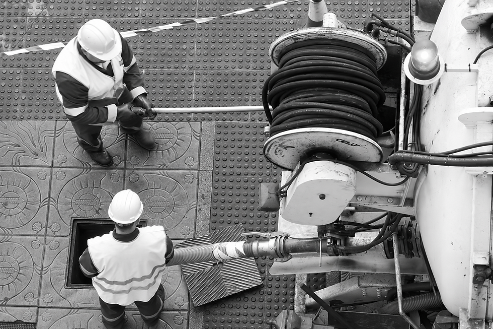 Two operatives wearing hard hats working with drain jetting equipment beside a tanker