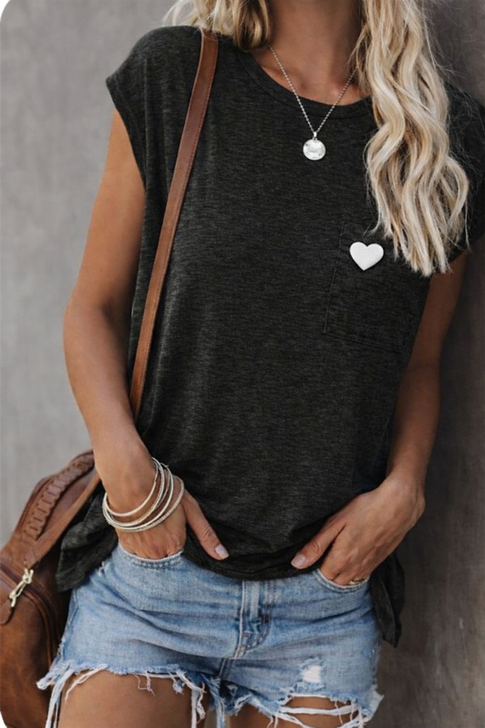 Pin's cœur blanc porté sur un t-shirt noir avec jean clair et sac bandoulière marron