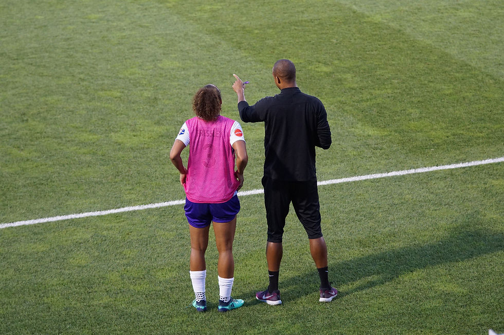 A football coach points while guiding a young player on the pitch, illustrating support for academy players’ mental health.