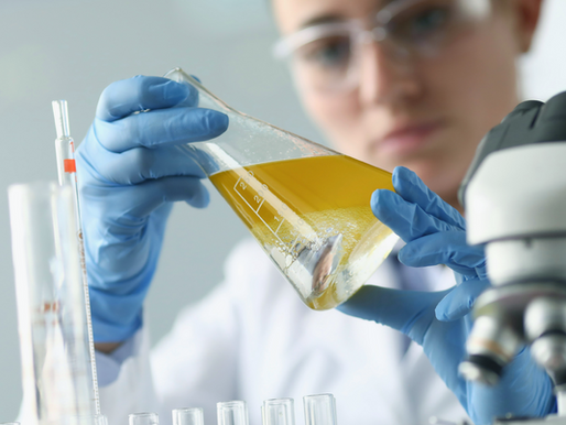 A scientist wearing gloves and goggles carefully examines a beaker with yellow liquid, surrounded by lab equipment, conveying focus and precision.