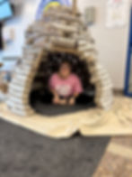 Smiling woman sitting inside a large igloo made of egg cartons.