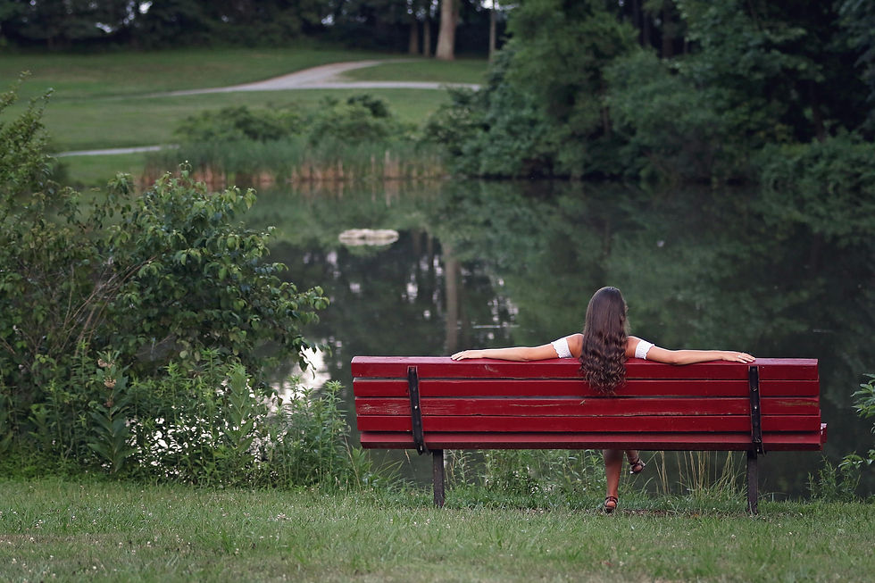 A woman sitting on a bench, looking at a pond