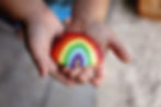 The hands of a young toddler child are gently holding an acrylic painted rainbow rock..jpg