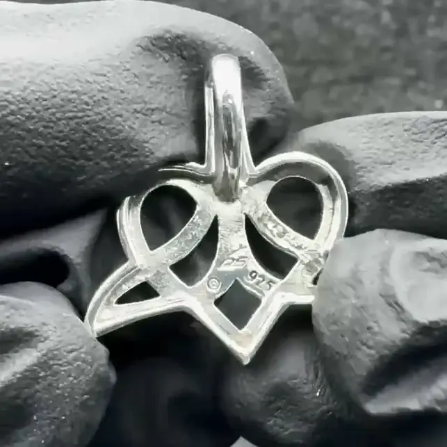 Thumbnail: Silver Celtic heart knot pendant with '925' mark held by gloved hands.