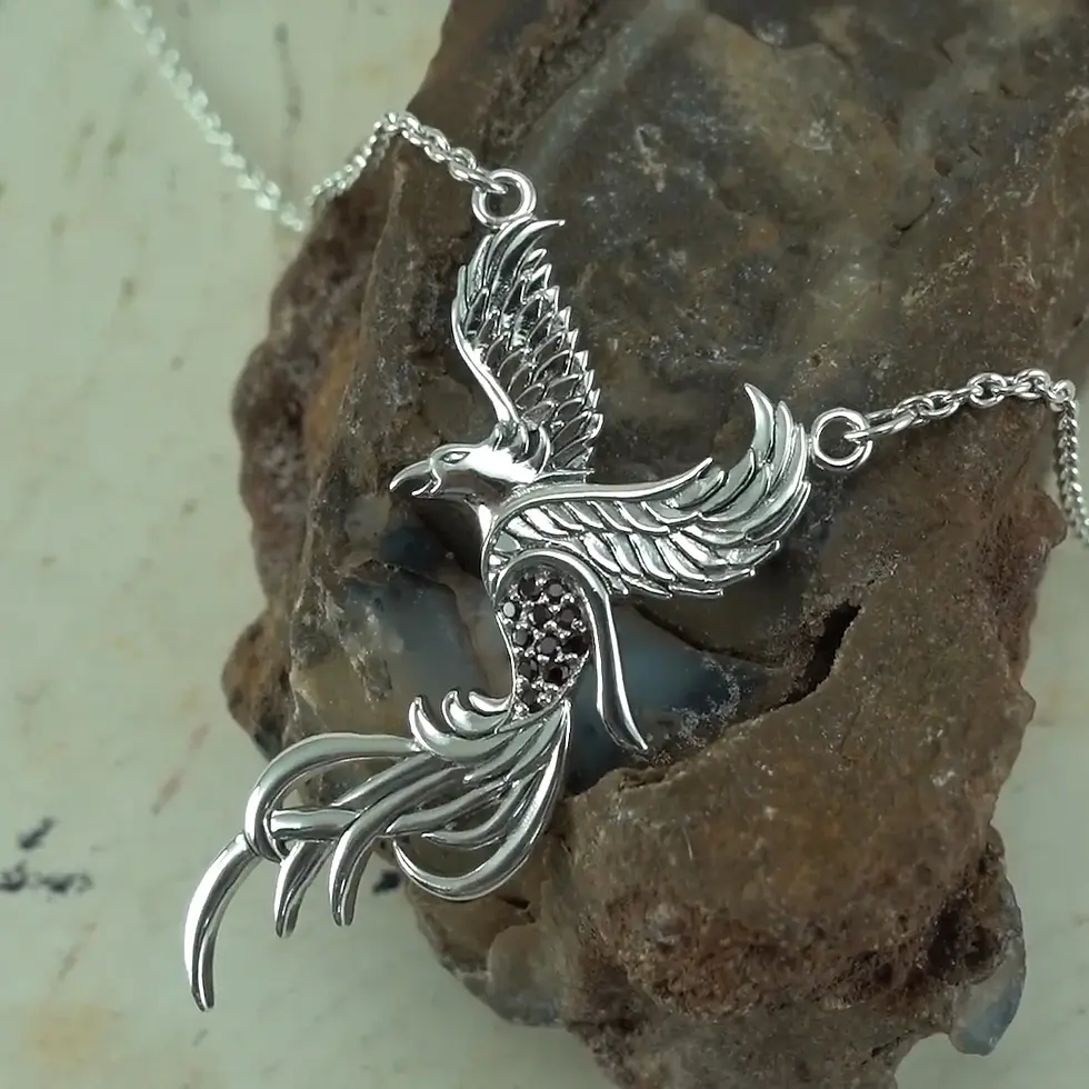Thumbnail: Intricate silver phoenix pendant with spread wings resting on dark stone.