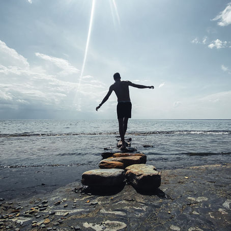 A person balancing on stones on a shoreline