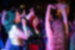 3 people dancing at a club with their arms up surrounded by neon lights.