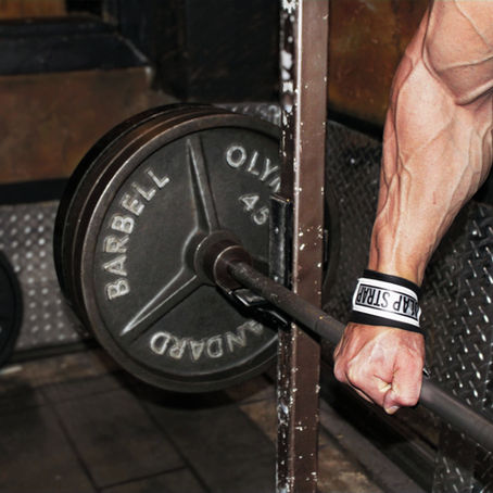 Strong bodybuilder using weight lifting straps to work out.