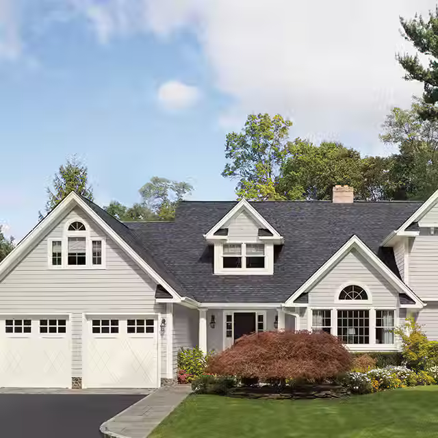 A large white house in the color White Wisp by Benjamin Moore, featuring a driveway and two garages, set against a clear blue sky.