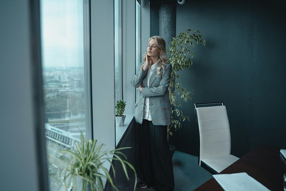 Thoughtful woman in a blazer stands by a large office window