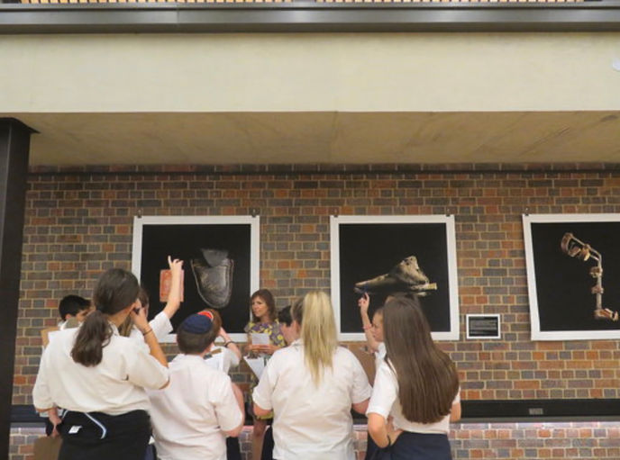 Students gathered around an adult in front of three artworks on a brick wall.