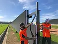 Concept Evolution technicians installing a tall black barrier fence, one using a level