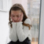 Child sitting alone by a window, looking out, representing isolation