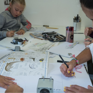 Kinder zeichnen eine Getränkedose und andere Gegenstände mit Bleistift als Übung zur Objektstudie.