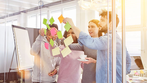 Mehrere junge Menschen kleben bunte Post-its an eine Glaswand – Symbol für Zusammenarbeit, neue Ideen und interaktive Finanzbildung in den Firmenseminaren von Christine Schremb