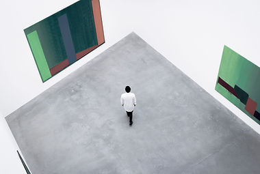 A man in a large art exibition space looking at a painting