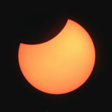golden yellow moon with a 'bite' out of it against a black 