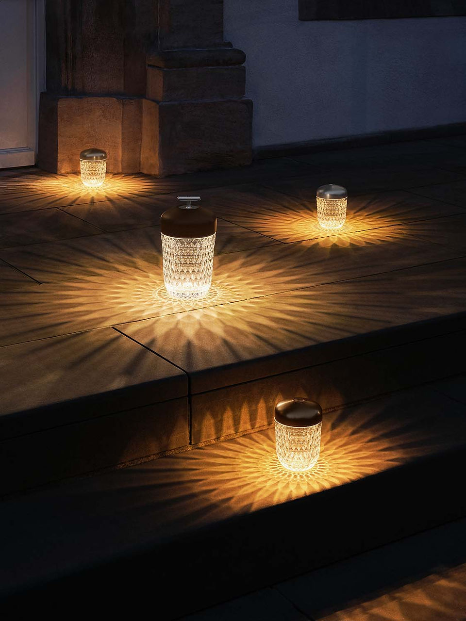 Photo shows one large Folia portable lamp, accompanied by three Mini Folia lamps, all illuminated in a warm white light setting