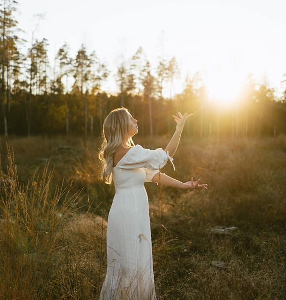 kvinna står på ett fält i solnedgången och healar