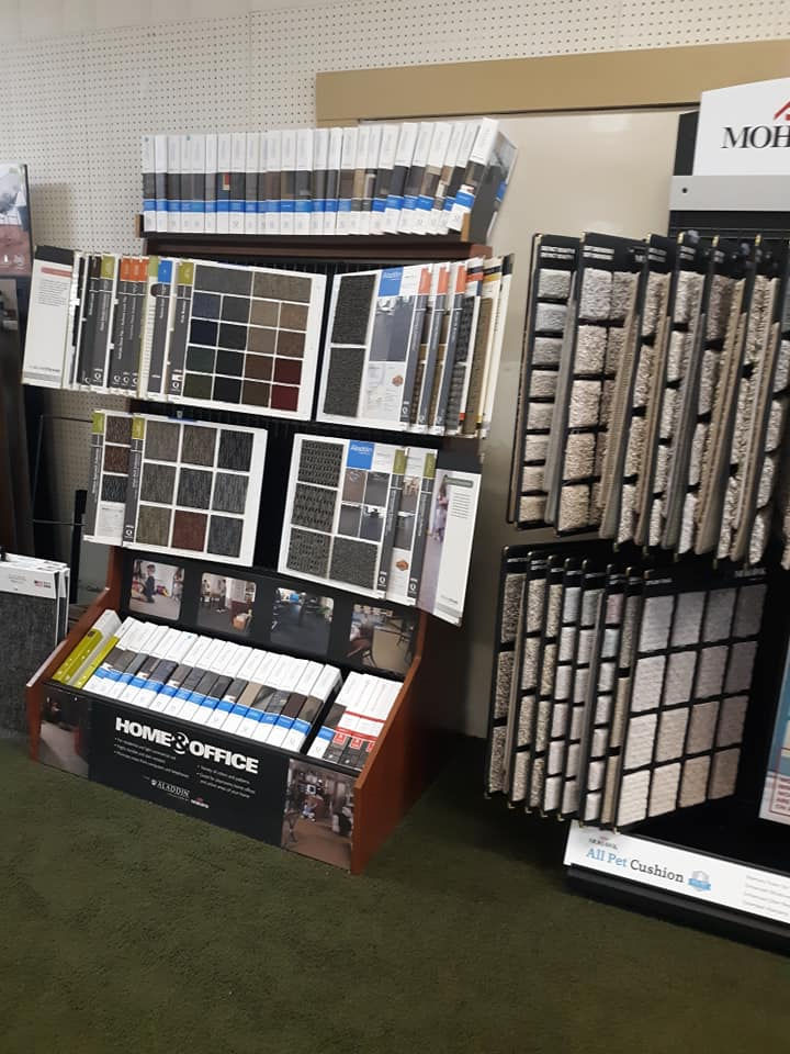 Display stand with various carpet and flooring samples, including color swatches and textured material samples, arranged in rows for customers to view and compare options for home and office use.