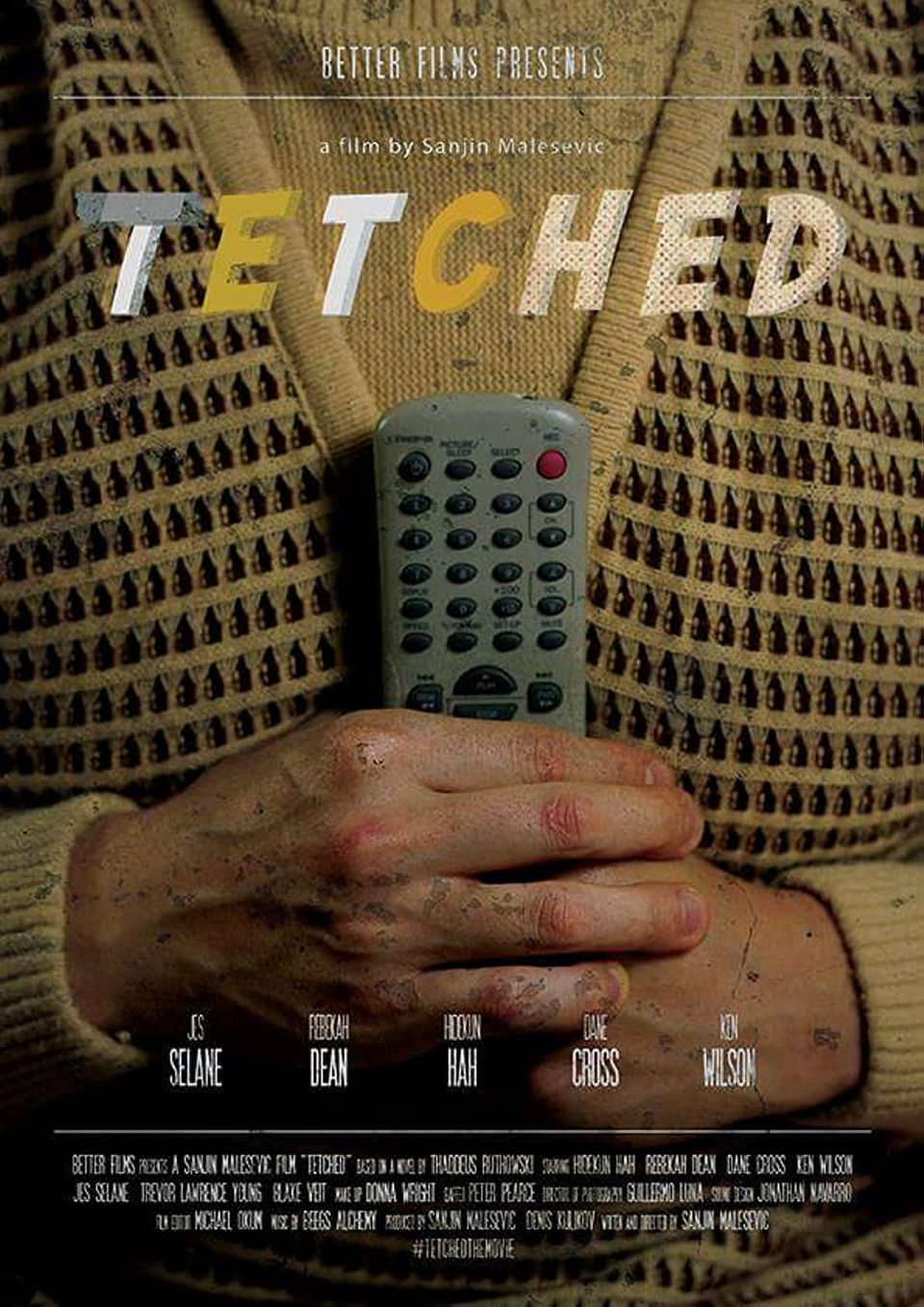 Torso of a man wearing a yellow patterned sweater as he clutches an old television remote 