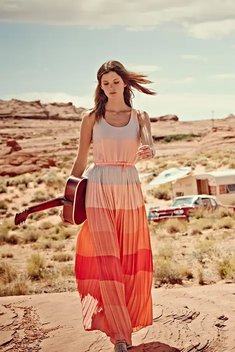 Woman in a long flowing orange and pink dress standing in a dry desert landscape. Captured by Thomas Hoeffgen.