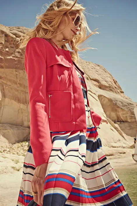 Woman in a bold red jacket and patterned skirt posed against a rocky outdoor backdrop. Shot by Thomas Hoeffgen.