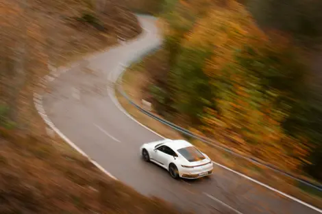 White sports car navigating a curved road through autumn foliage with motion blur. Photographed by Thomas Hoeffgen.