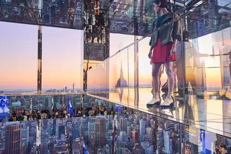Person in casual clothing standing on a mirrored glass observation deck with city skyline reflections at dusk. Captured by Thomas Hoeffgen in New York.