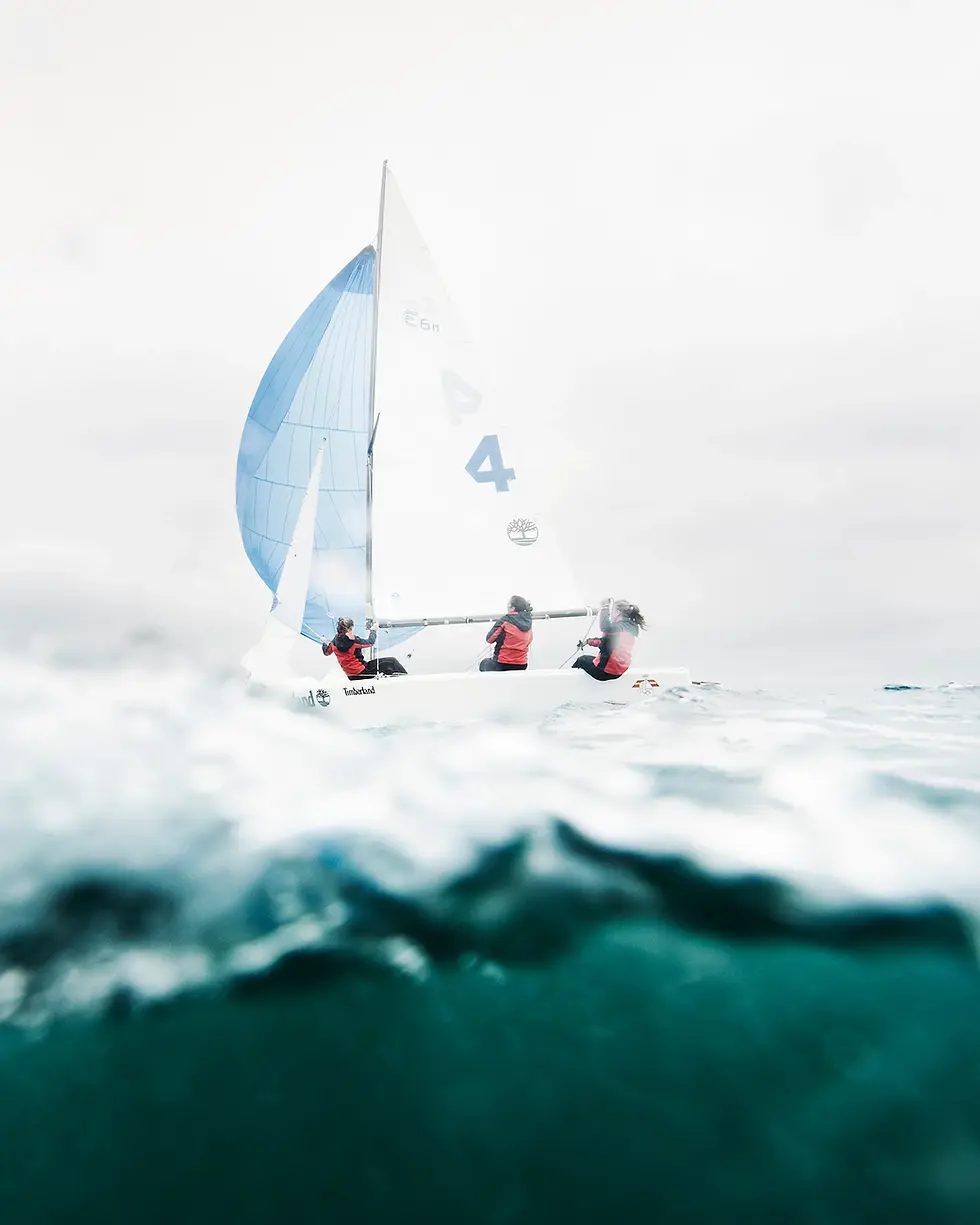 Sailboat with white and blue sails cutting through deep blue ocean water under a cloudy sky. Shot by Thomas Hoeffgen.