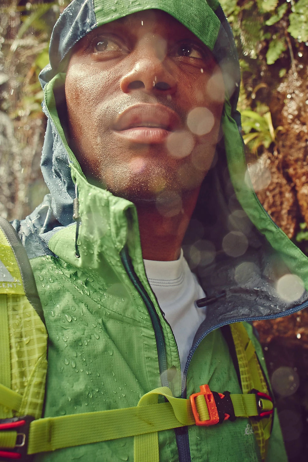 Man in a bright green rain jacket hiking in a lush outdoor setting. Photographed by Thomas Hoeffgen.