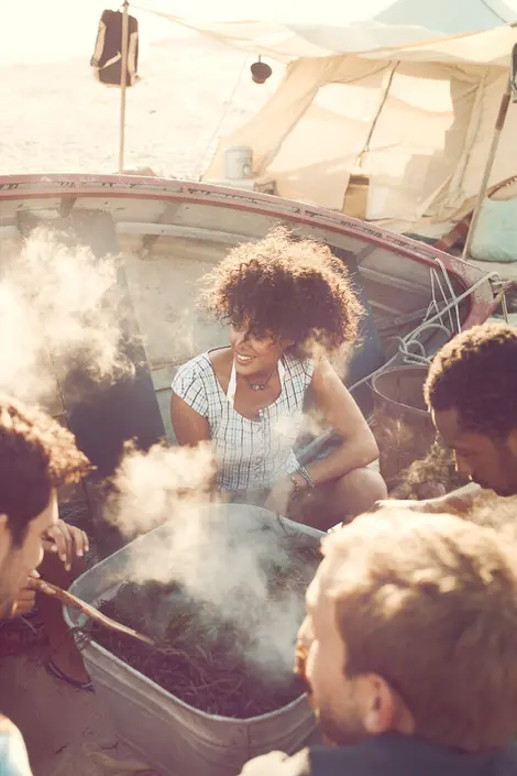 Group of people in casual clothing gathered around a campfire in a beach landscape. Photographed by Thomas Hoeffgen.
