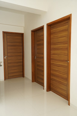 Hallway with three modern horizontal-grain wooden doors and sleek metal handles in a minimalist interior by wooden door manufacturers in Ahmedabad, Gujarat.