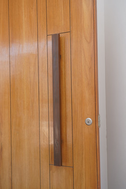 Close-up of vertical-panel veneer modular wooden door with sleek long handle and keyhole detail by Veneer modular doors for apartments manufacturers in Ahmedabad.