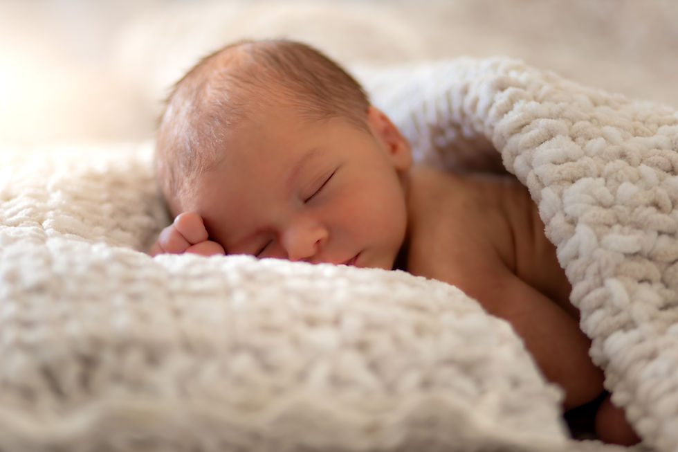 Newborn baby sleeping, fist balled up by face, white blankets and super cute.